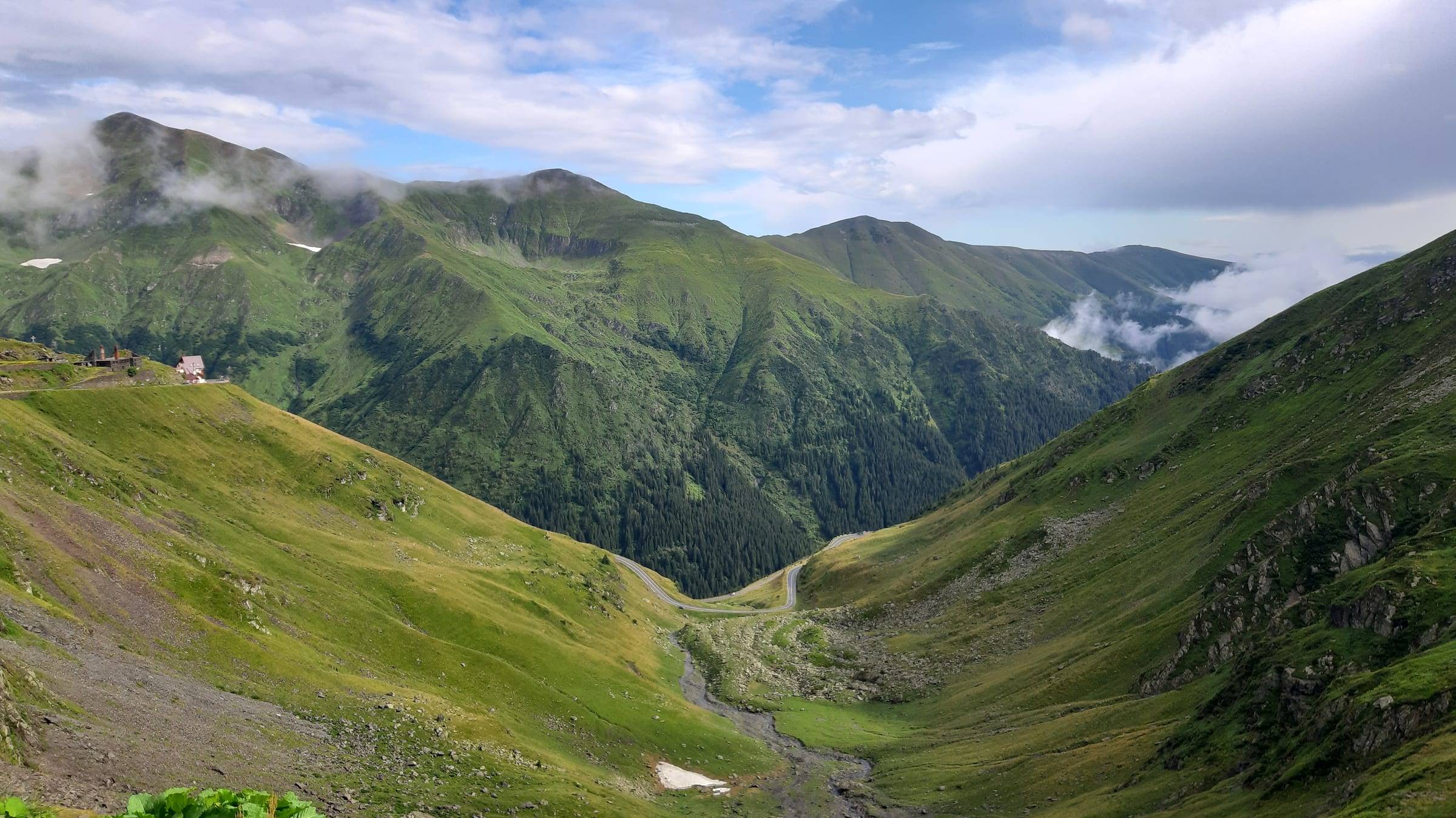 Vale montană verde, cu nori deasupra crestelor